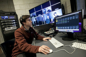 A male student uses a computer for film and media studies with monitors in the background