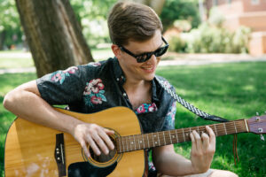 Chris Ulyett plays an acoustic guitar outdoors.