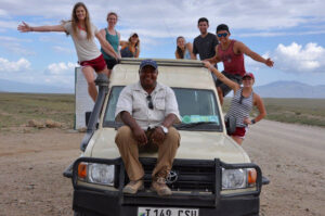 Seven students and a driver pose on a Jeep