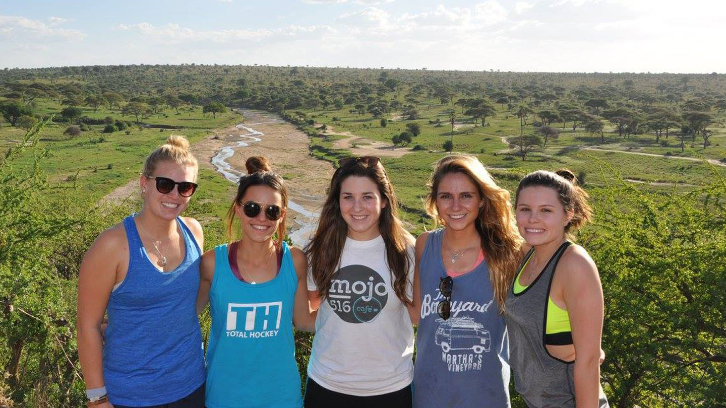 A group of five women students pose for a photo in a Tanzania wildlife preserve.