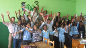 Students raise their hands in a classroom while posing for a photo.